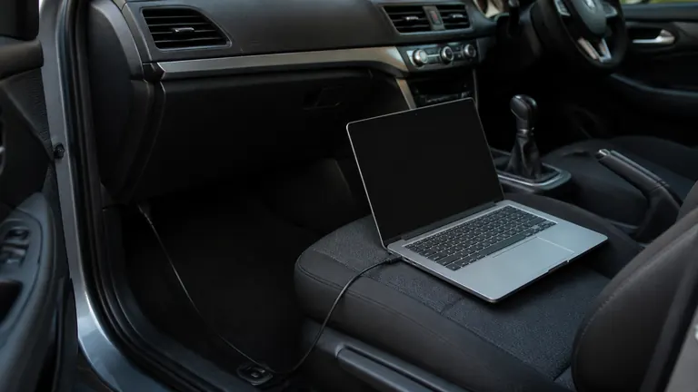 Laptop on a car seat with a cable running toward the footwell